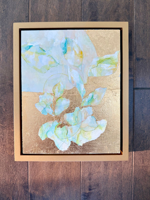 Framed abstract artwork with floral design and gold foil on a wooden surface